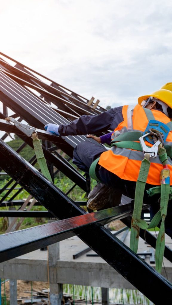 Travailleur de la construction portant un harnais de sécurité et utilisant un dispositif de sécurité secondaire se connectant à une corde statique de 15 mm utilisée comme bardeau de retenue de chute au sommet du nouveau toit.